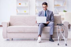 businessman on crutches with a broken leg home working